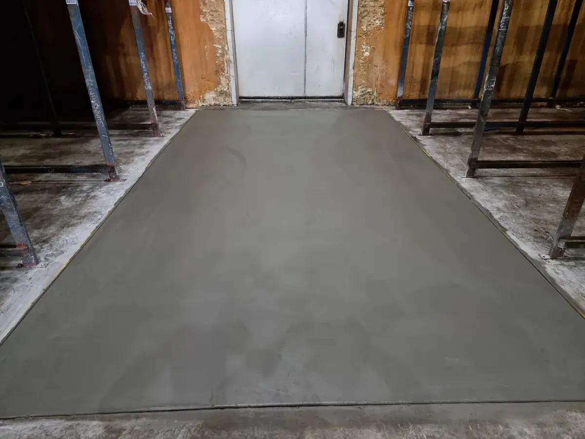 Replaced section of concrete floor, finished flush, between steel racking frames in front of an insulated door
