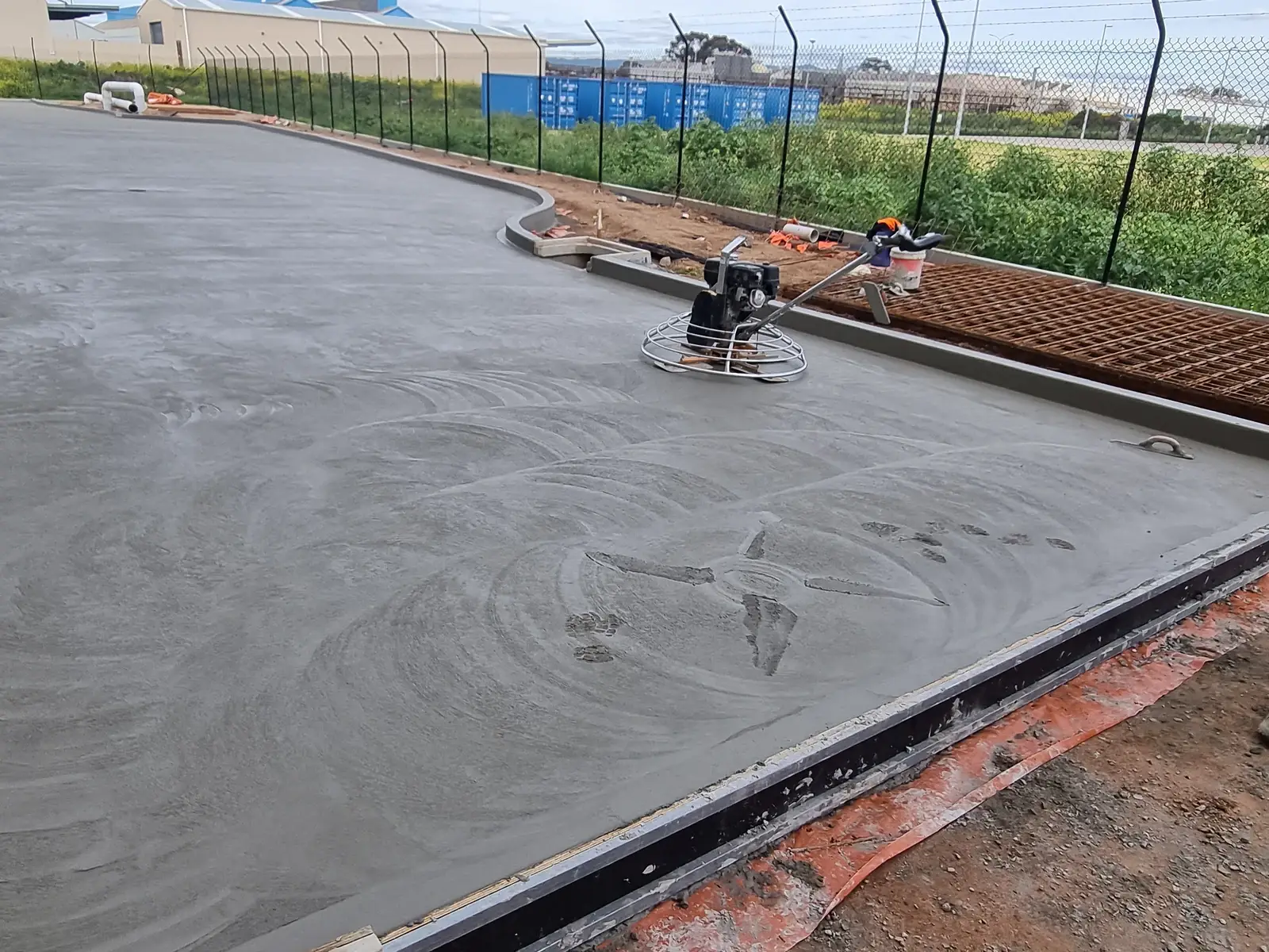 Freshly poured concrete roadway and kerb at an industrial site in Wingfield, with a power trowel finishing the slab